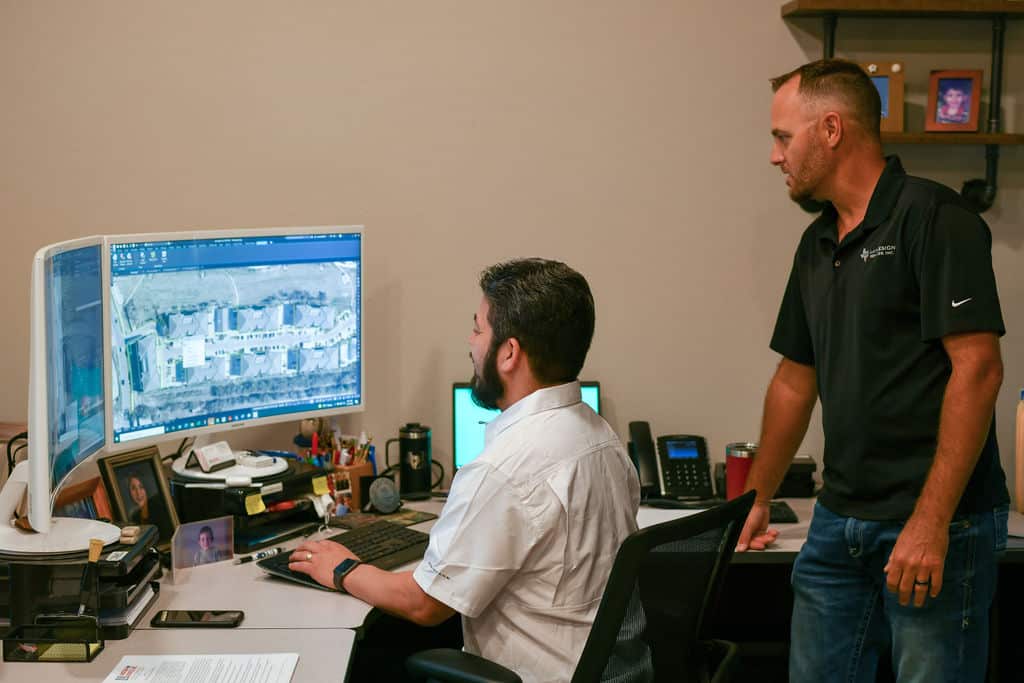 Two land survey professionals watching computer screen and reviewing data from land survey on digital platform