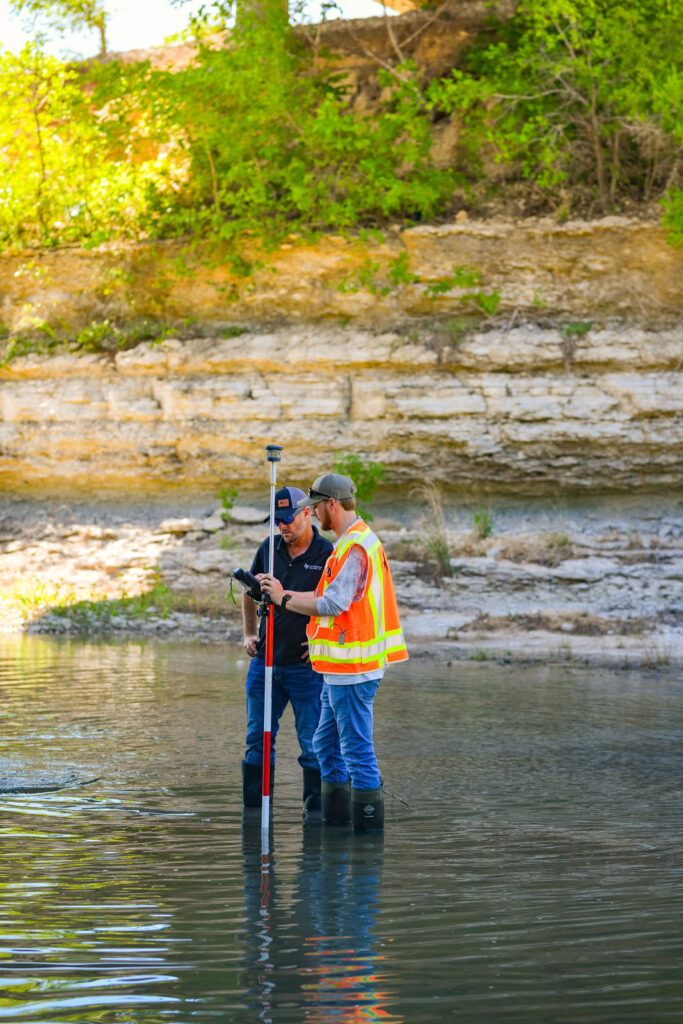 land survey technicians standing in river with mud boots reading survey data for bridge and land survey solutions